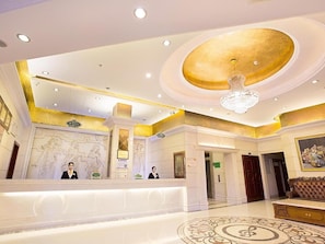 A hotel lobby with a reception desk, a chandelier, and a large mural on the wall. - Vienna Hotel (Chengdu)