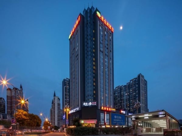 A high-rise building with illuminated signage, surrounded by other tall buildings and a clear sky. - Vienna Hotel (Chengdu)
