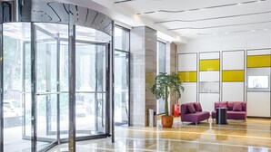 A modern lobby with a glass door entrance, a potted plant, and purple seating. - Lavande Hotel (Ganzhou)