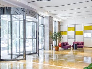 A modern lobby with a glass door entrance, a potted plant, and purple seating. - Lavande Hotel (Ganzhou)