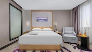A hotel room with a large bed, a chair, a small table with fruit, and a painting on the wall. - Lavande Hotel (Ganzhou)