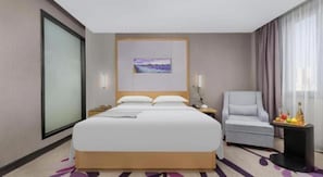 A hotel room with a large bed, a chair, a small table with fruit, and a painting on the wall. - Lavande Hotel (Ganzhou)