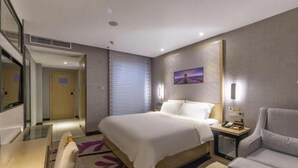 A hotel room with a bed, bedside table, chair, and a painting on the wall. - Lavande Hotel (Ganzhou)