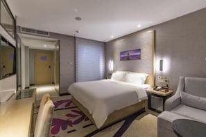 A hotel room with a bed, bedside table, chair, and a painting on the wall. - Lavande Hotel (Ganzhou)