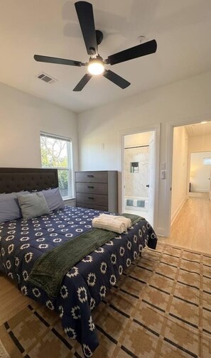A bedroom with a bed, a ceiling fan, a dresser, and a bathroom door. - Modern 2BR Townhome | Medical Center • NRG • Hobby (Houston)