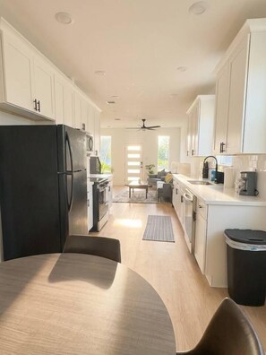 A modern kitchen with white cabinets, a black refrigerator, and a dining area with a table and chairs. - Modern 2BR Townhome | Medical Center • NRG • Hobby (Houston)