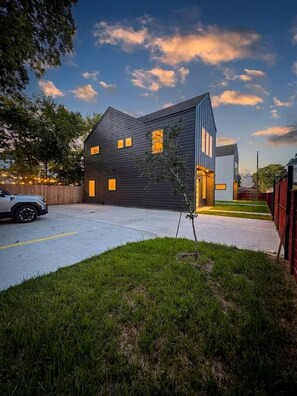 A modern two-story house with a driveway and a small lawn area. - Modern 2BR Townhome | Medical Center • NRG • Hobby (Houston)