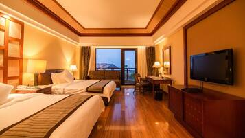 A hotel room with two beds, a desk, a television, and a view of the outside.