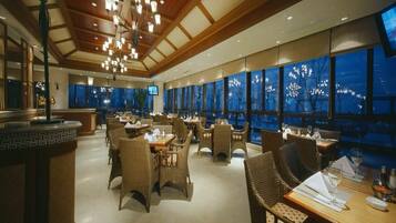 A restaurant with high ceilings, chandeliers, and large windows offering a view of the cityscape.
