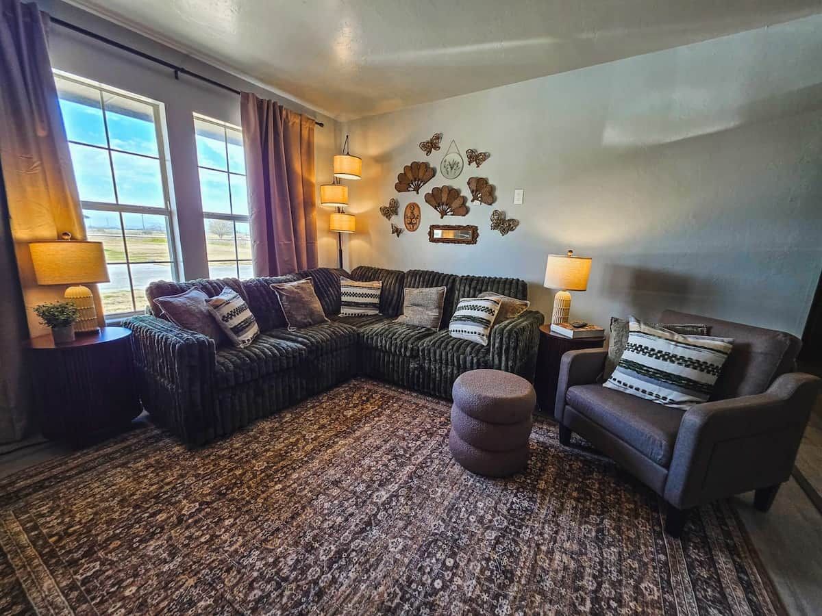 A living room with a sectional sofa, a round ottoman, a chair, and a patterned rug.