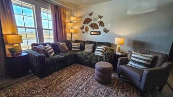 A living room with a sectional sofa, a round ottoman, a chair, and a patterned rug.