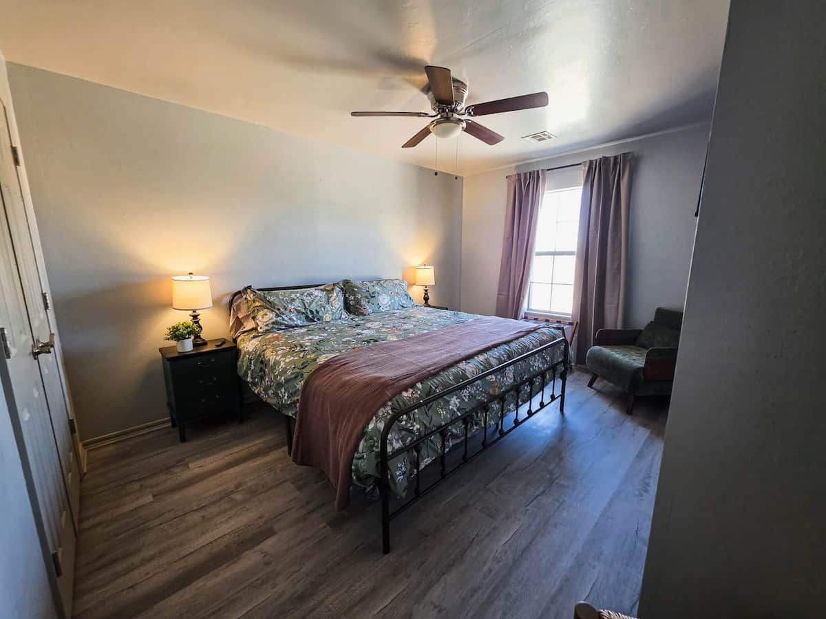 A bedroom with a bed, bedside lamps, a ceiling fan, and a window with curtains.