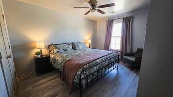 A bedroom with a bed, bedside lamps, a ceiling fan, and a window with curtains.
