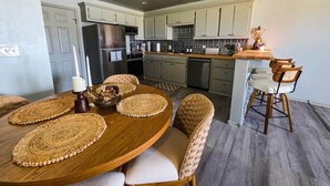 A modern kitchen with a dining area, featuring a wooden table, woven placemats, and wicker chairs. - FamilyFriendly 2BR,King bed @ Fort Sill & Lawton #1 (Elgin)
