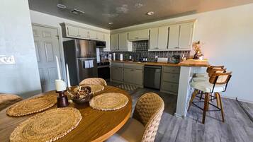 A modern kitchen with a dining area, featuring a wooden table, woven placemats, and wicker chairs.