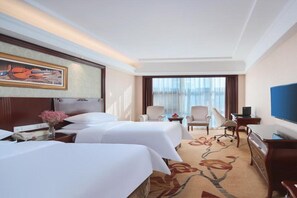 Habitación de hotel con dos camas, televisión, escritorio y un ventanal grande.