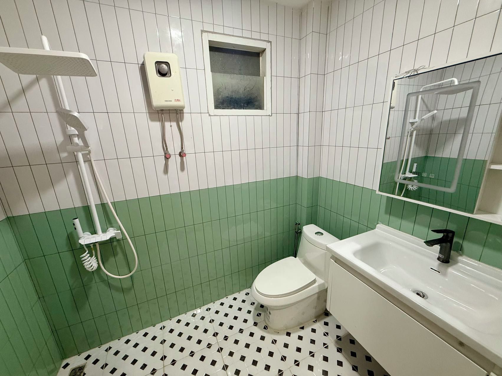Une salle de bain équipée d’un WC, d’un lavabo, d’une douchette et d’un miroir.