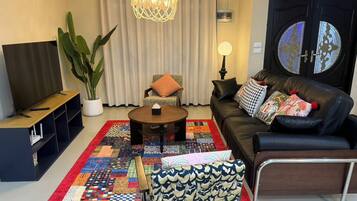 A living room with a sofa, coffee table, TV, and a large plant.