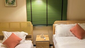 Una camera d'albergo con due letti, un comodino con una lampada, un quadro appeso alla parete e una finestra con persiane verdi.