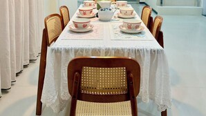 Zona pranzo con tavolo apparecchiato per quattro, circondata da sedie in vimini, un lampadario decorativo e una scala che conduce a un piano superiore.