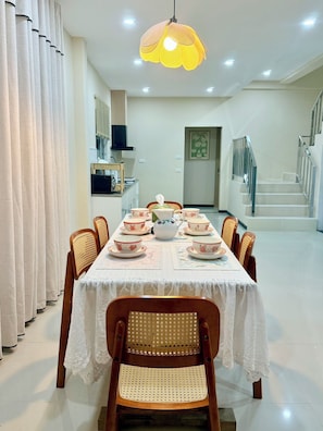 A dining area with a table set for four, surrounded by wicker chairs, a decorative hanging light fixture, and a staircase leading to an upper level. - Moon house 5BR Near Walking Street  (Nongprue)