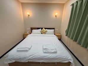 A neatly made bed with white linens and two towels, a bedside table with a lamp, and a green curtain on the window. - Moon house 5BR Near Walking Street  (Nongprue)