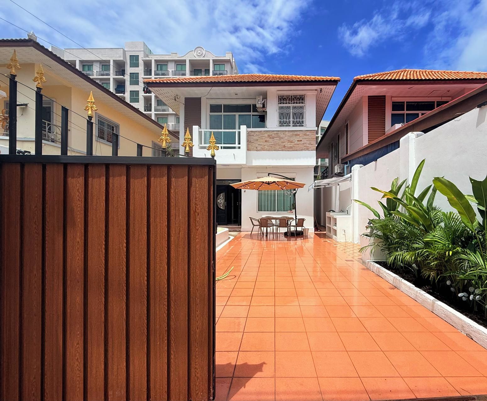 Un quartier résidentiel doté d’une terrasse carrelée, d’une clôture en bois et d’un coin repas avec des chaises et un parasol.