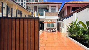 A residential area with a tiled patio, a wooden fence, and a dining area with chairs and an umbrella.