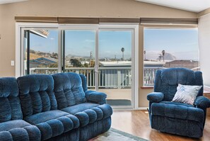 A balcony with a sliding glass door, a blue armchair, and a sofa. - 3 bedroom beach view home in Morro Bay! Room for the family- medium term rental (Morro Bay)