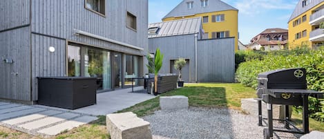 A modern residential building with a patio area, outdoor seating, and a barbecue grill.