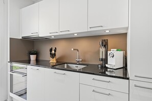 Een moderne keuken met witte kastjes, een zwart aanrecht en roestvrijstalen apparatuur.