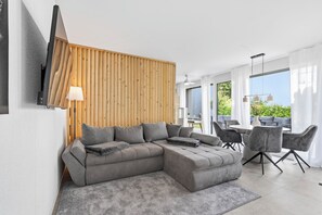 Een moderne woonkamer met een hoekbank, een wand van hout, een flatscreen tv aan de muur en een eethoek met een tafel en stoelen.