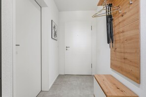 A hallway with a wooden bench, a coat rack with hangers, and a door with a small picture on the wall.