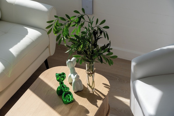 A room with a white sofa, a round wooden coffee table, a glass vase with green plants, and two ceramic animal figurines.