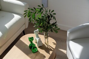 A room with a white sofa, a round wooden coffee table, a glass vase with green plants, and two ceramic animal figurines.