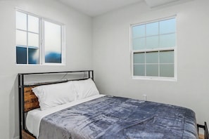 A bedroom with a bed, two windows, and a wall socket.