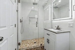 Un bany modern amb dutxa de vidre, un lavabo amb rentapèns i un mirall gran.