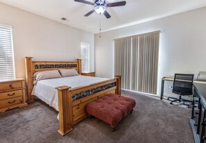 A bedroom with a wooden bed, a red bench, a desk with a chair, and a ceiling fan.