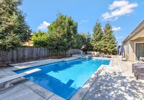 A rectangular swimming pool with a wooden fence and trees around.