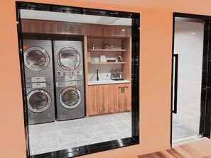 Une buanderie équipée de deux machines à laver et d’un étendoir, d’une armoire en bois et d’une petite étagère où sont rangés divers objets.