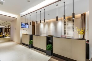 A modern reception desk with a flat-screen TV, pendant lights, and potted plants. - Home Inn Plus Shanghai Pudong Jinqiao (Shanghai)