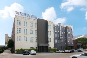 Un hôtel à la façade moderne, avec de nombreux  étages et un parking où sont garées plusieurs voitures.