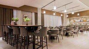 Un espace repas moderne avec une longue table et de nombreuses chaises, un coin bar avec des tabourets et une cuisine en arrière-plan.