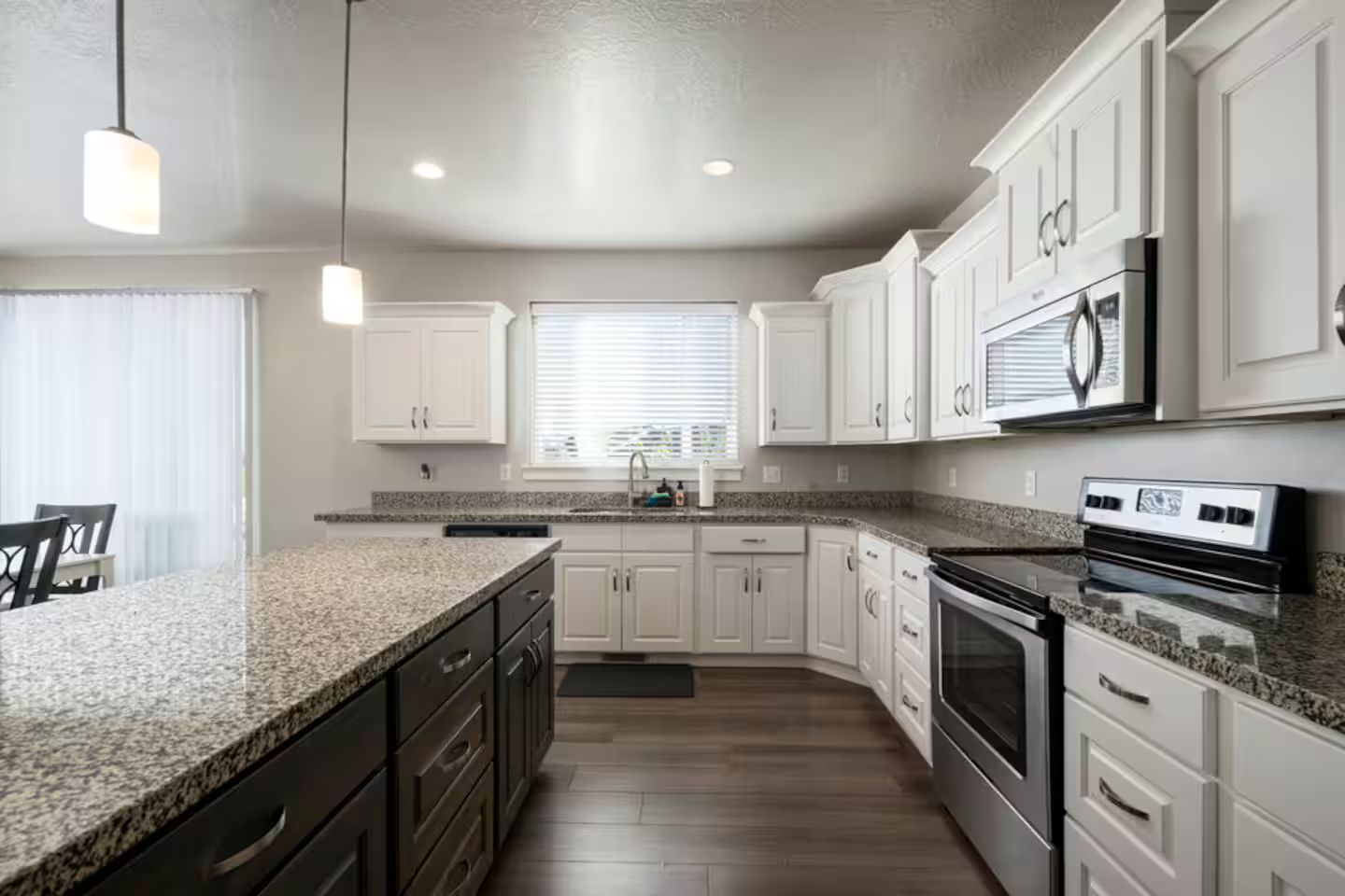 A kitchen with granite countertops, white cabinetry, a built-in oven, and a window with blinds.