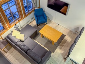A modern living room with a grey sofa, a blue armchair, a wooden coffee table, and a TV mounted on the wall. - Renovated 2 BD+ loft by the lake, free wifi, sauna (Kuusamo)