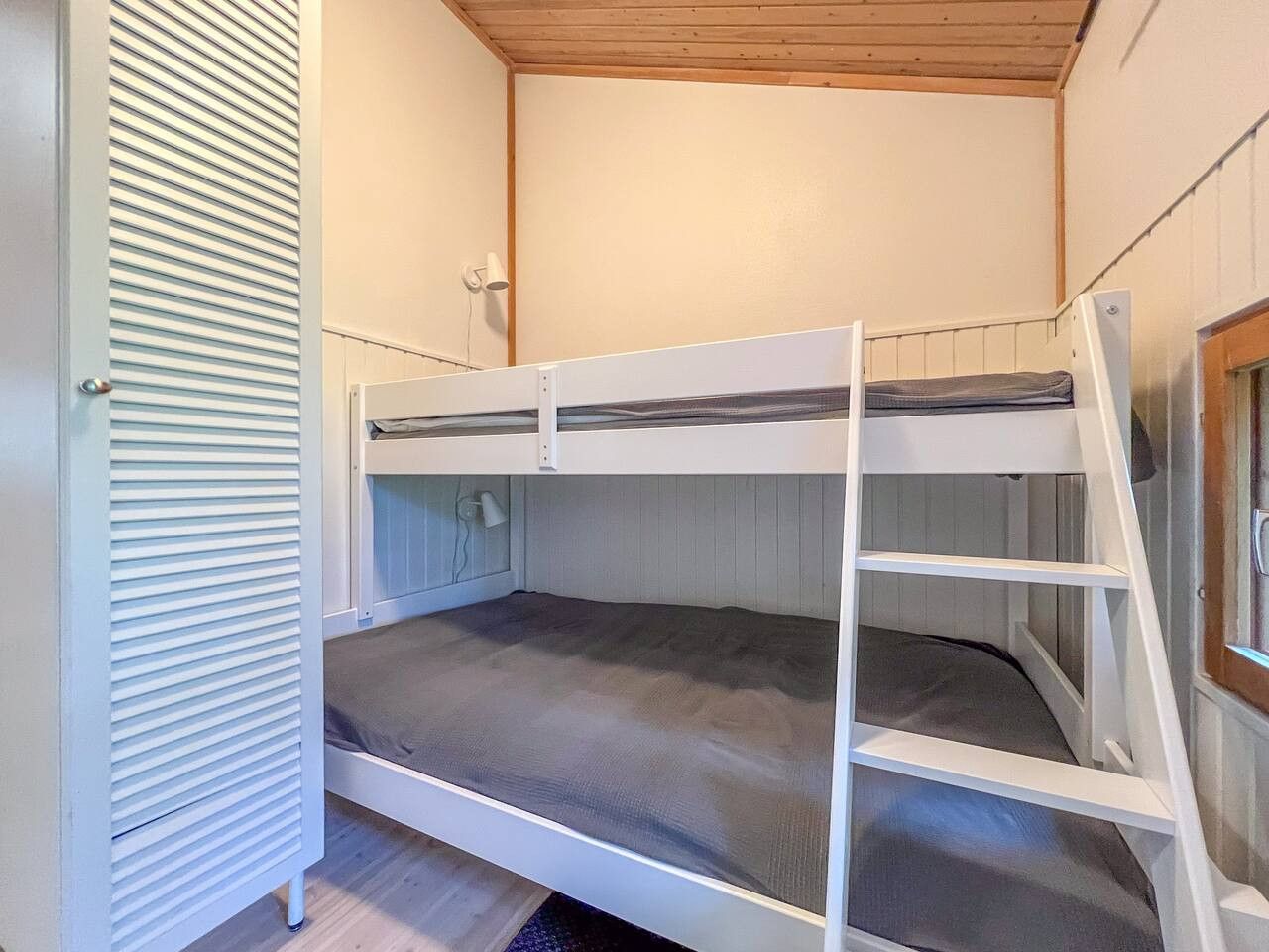 A bunk bed with a ladder, a wall-mounted lamp, and a window.