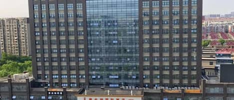 Un hotel de varios pisos con fachada de vidrio moderna, una entrada destacada con un letrero y un área de estacionamiento al frente.