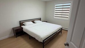 Un dormitorio con cama, mesita de noche, ventana con persianas y puerta.