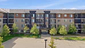 Un edificio de apartamentos moderno de varios pisos, número 7210, con balcones y un área de estacionamiento al frente.