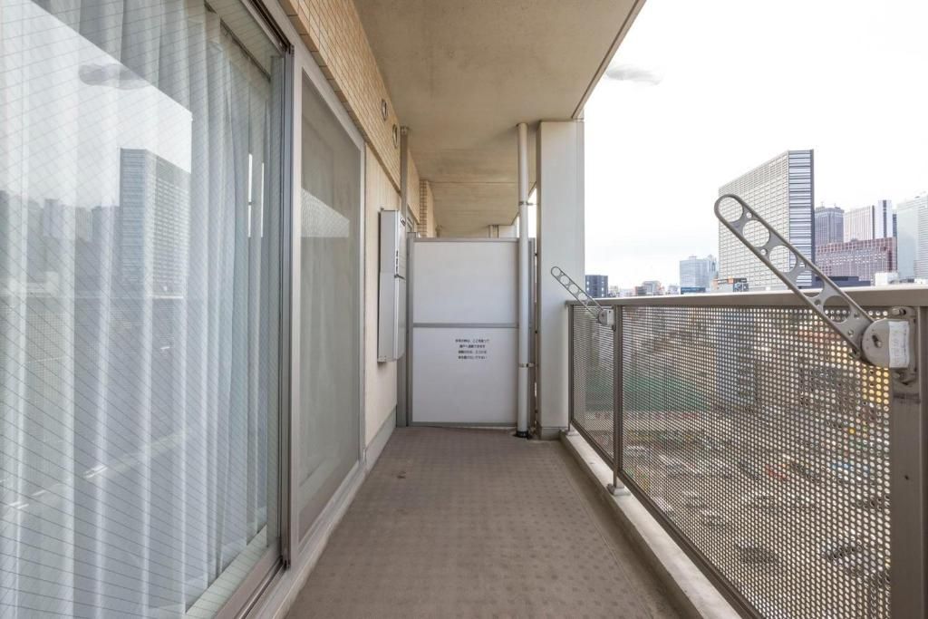 Un corridoio stretto con una ringhiera metallica, una porta con un cartello e una vista sulla città sullo sfondo.